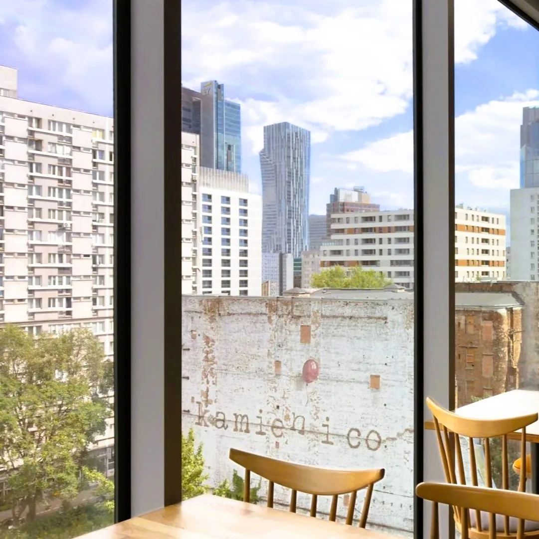 Sala śniadaniowa na 7. piętrze ibis Styles Warszawa City — panoramiczne okna od podłogi do sufitu, stoliki przy szybie i widok na centrum Warszawy oraz przedwojenną kamienicę przy ul. Waliców
